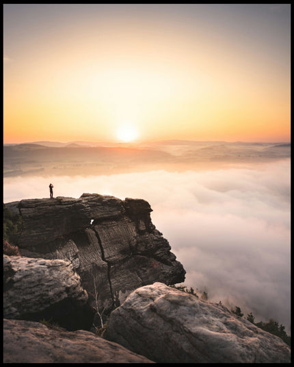 Ein Leinwandbild von einem Bergsteiger, der bei Sonnenaufgang auf einer Klippe steht.