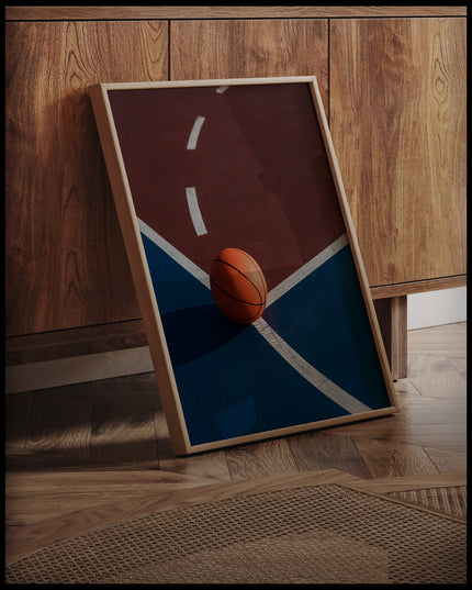 Ein gerahmtes Poster von einem Basketball auf einem Basketballplatz mit roten und blauen Feldern, an einer Holzkommode angelehnt und stehend auf dem Holzboden