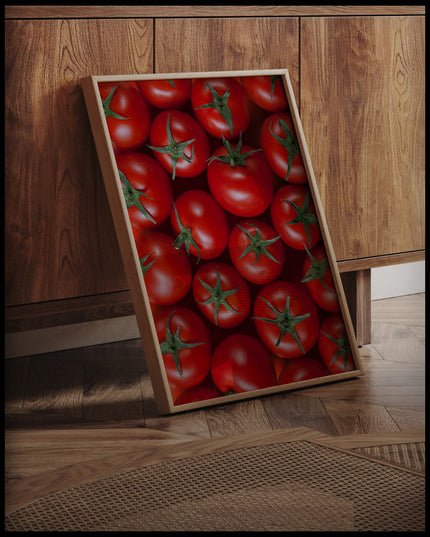 Ein gerahmtes Poster einer Nahaufnahme von mehreren Tomaten, an einer Holzkommode angelehnt und stehend auf dem Holzboden