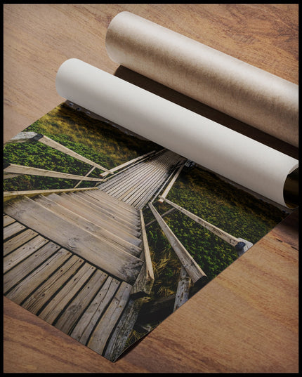 Ein Poster von einem Holzsteg mit einer Treppe, der durch Dünen zum Strand führt, gerollt auf einer Holzoberfläche liegend