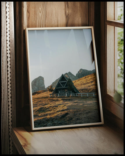 Ein gerahmtes Poster von einer kleinen Kapelle in den Dolomiten bei Sonnenuntergang, vor einem Fenster an die Wand angelehnt