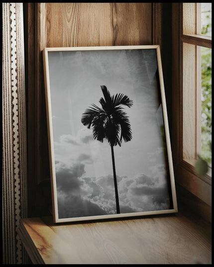 Ein gerahmtes Poster von einer einsamen Palme vor bewölktem Himmel in Schwarz-Weiß, vor einem Fenster an die Wand angelehnt