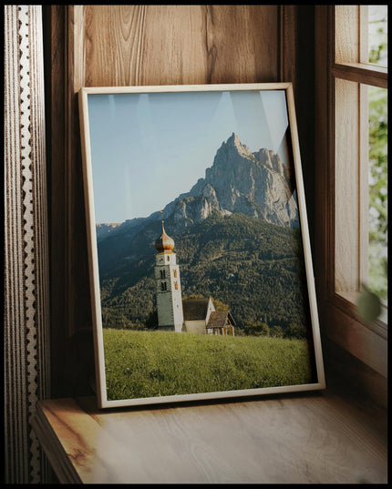 Ein gerahmtes Poster von einer Kirche am Abhang eines Berges in den Dolomiten, vor einem Fenster an die Wand angelehnt