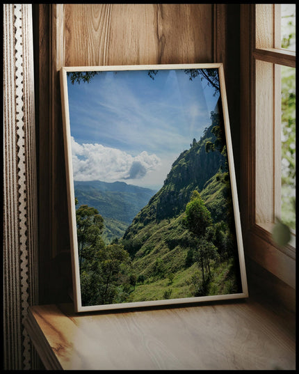 Ein gerahmtes Poster einer bewaldeten Berglandschaft in einer tropischen Region, vor einem Fenster an die Wand angelehnt