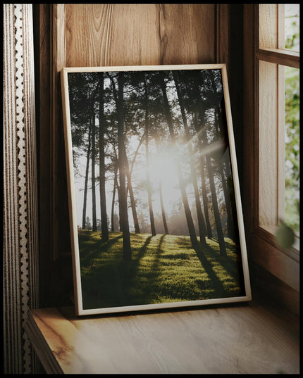 Ein gerahmtes Poster von Sonnenstrahlen die durch einige schmale Bäume hindurch scheinen, vor einem Fenster an die Wand angelehnt