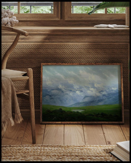 Ein gerahmter Kunstdruck von Wolken, die über die saftigen Wiesen einer Gebirgslandschaft ziehen, vor einem Fenster an die Wand angelehnt